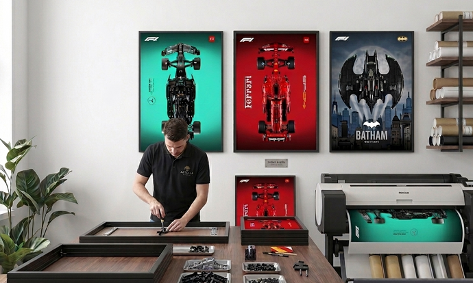Vue de l'atelier Astella Bricks montrant un artisan assemblant un cadre technique. Au mur, trois cadres 50x70cm (Mercedes F1, Ferrari et Batwing) illustrent la qualité d'impression haute définition et la robustesse du système de fixation.